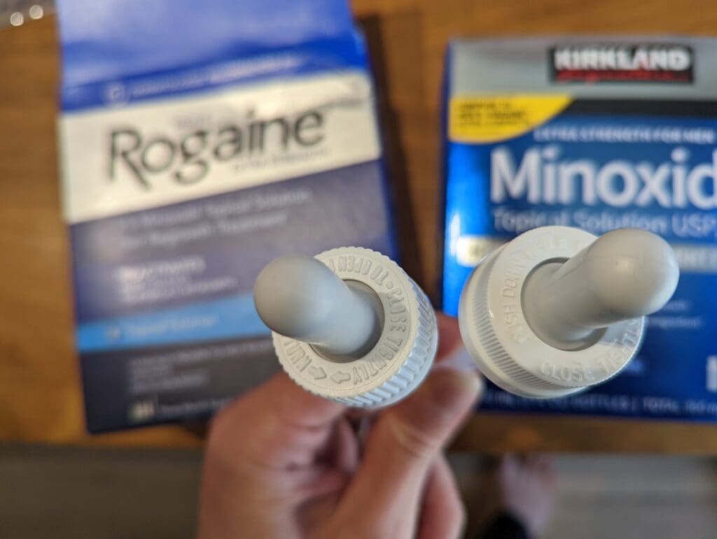 Rogaine 落建與 Kirkland 生髮水原廠滴管實體對比特寫:左側為 Rogaine,右側為 Kirkland。背景為各自的品牌外盒,展示 滴管頂部的不同。