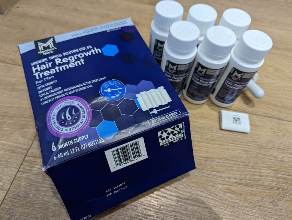 Member's Mark 生髮水開箱，旁邊擺放 6 罐未拆封的白色瓶身生髮水溶液，以及 1 支帶有刻度的原廠塑膠滴管。