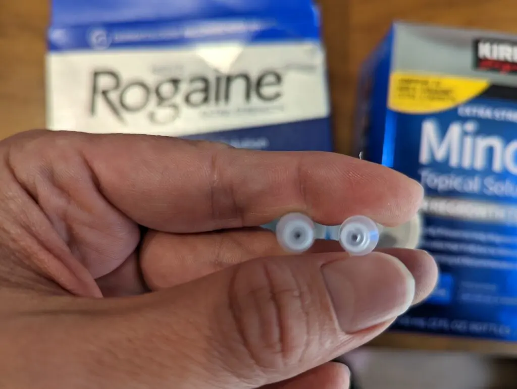 Rogaine 落建與 Kirkland 生髮水原廠滴管實體對比特寫：左側為 Rogaine，右側為 Kirkland。背景為各自的品牌外盒，展示滴管口的不同。