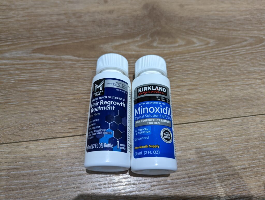 Member's Mark 生髮水 (左) 與 Kirkland 柯克蘭生髮水 (右) 單瓶正面平放對比，展示兩者皆為 60ml 的 5% Minoxidil 溶液。