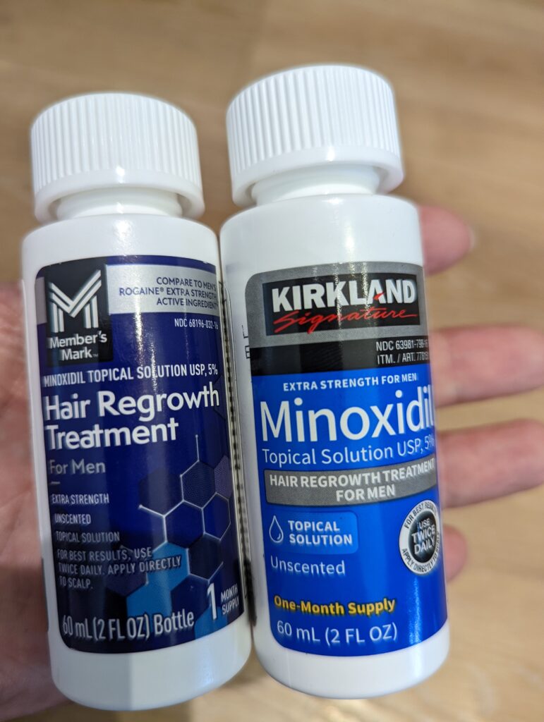 單手持 Member's Mark 生髮水與 Kirkland 生髮水進行近距離特寫對比，清楚可見兩者的 5% Minoxidil 標示。